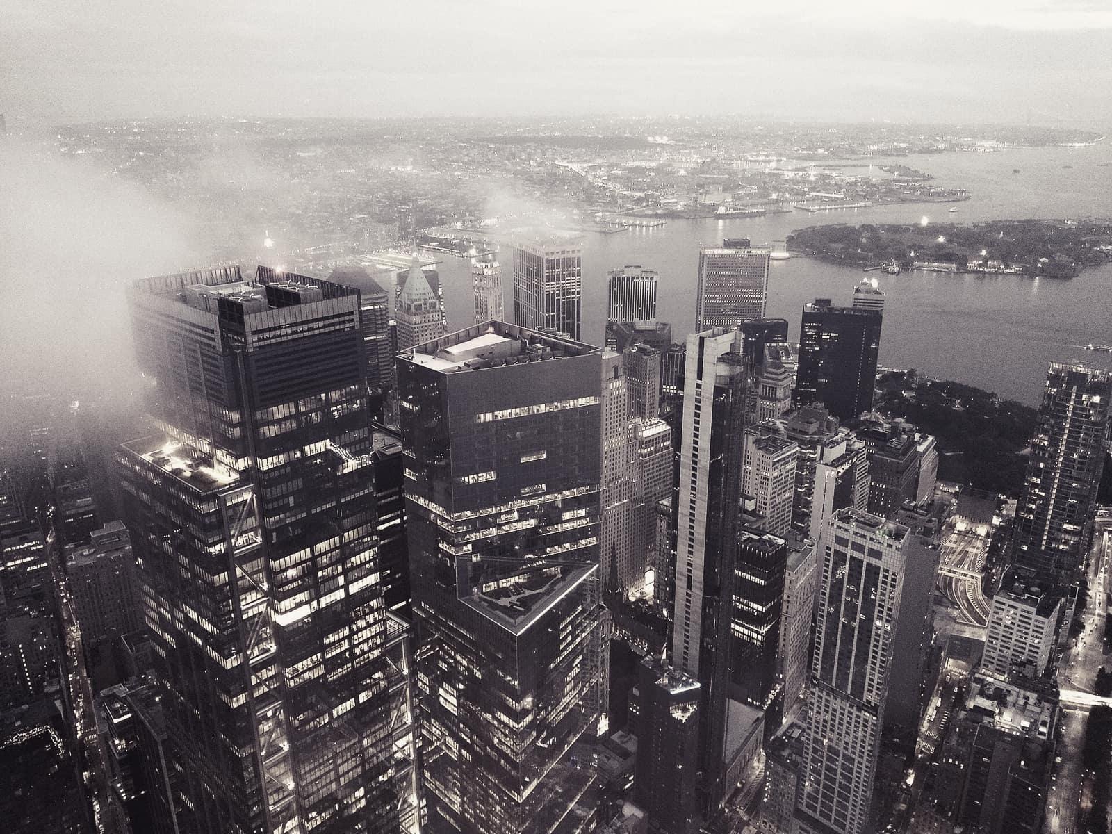 Office towers lit at dusk, seen from above with low cloud