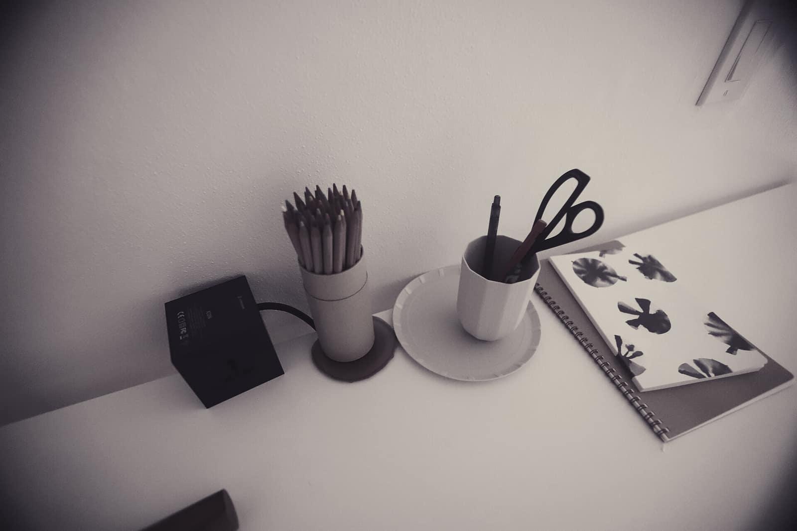 A minimal white desk with pencils in a holder and a notebook