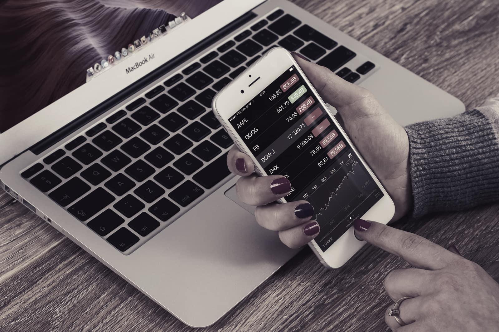 Checking share prices on a phone beside a laptop