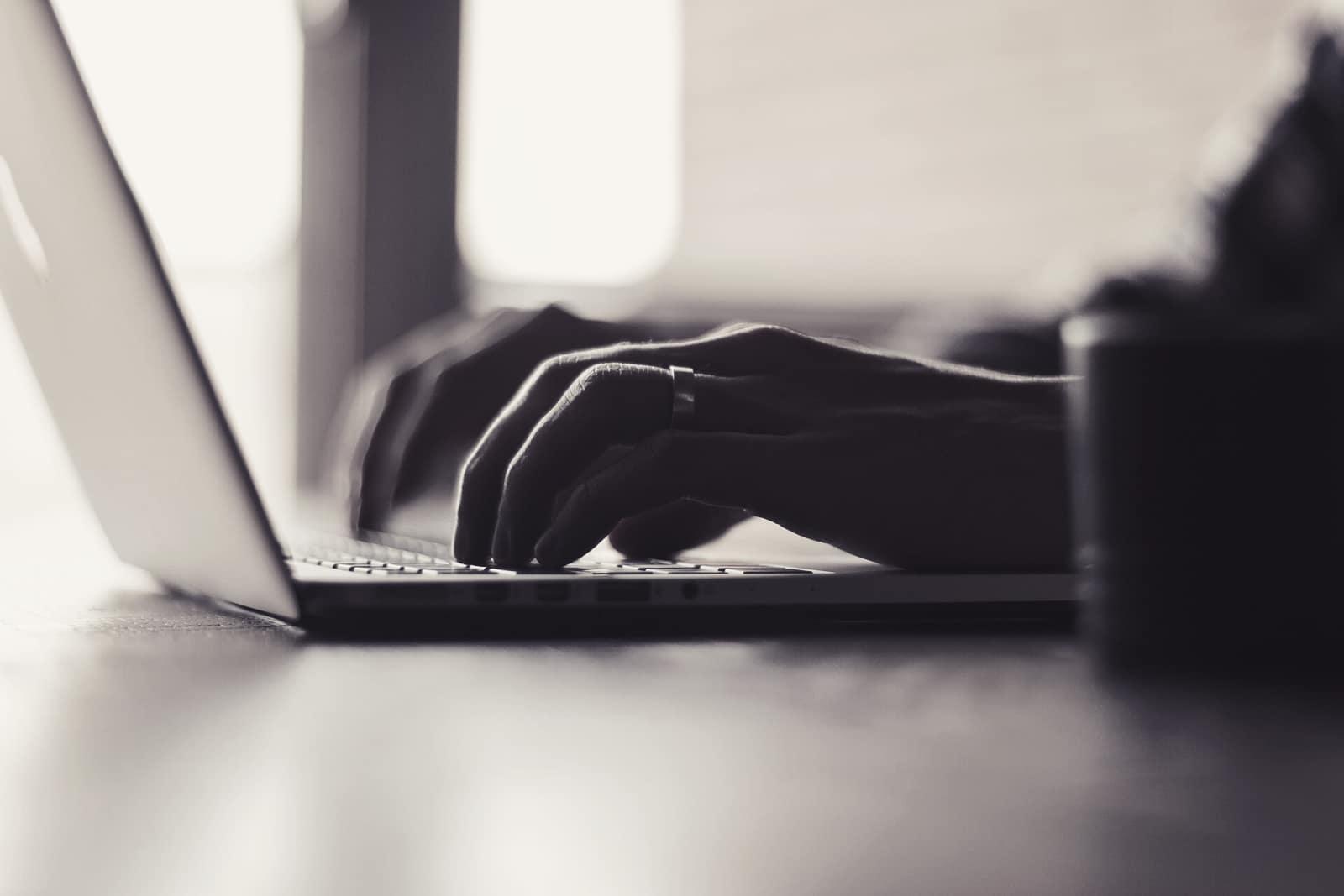 Hands typing on a laptop keyboard in low light