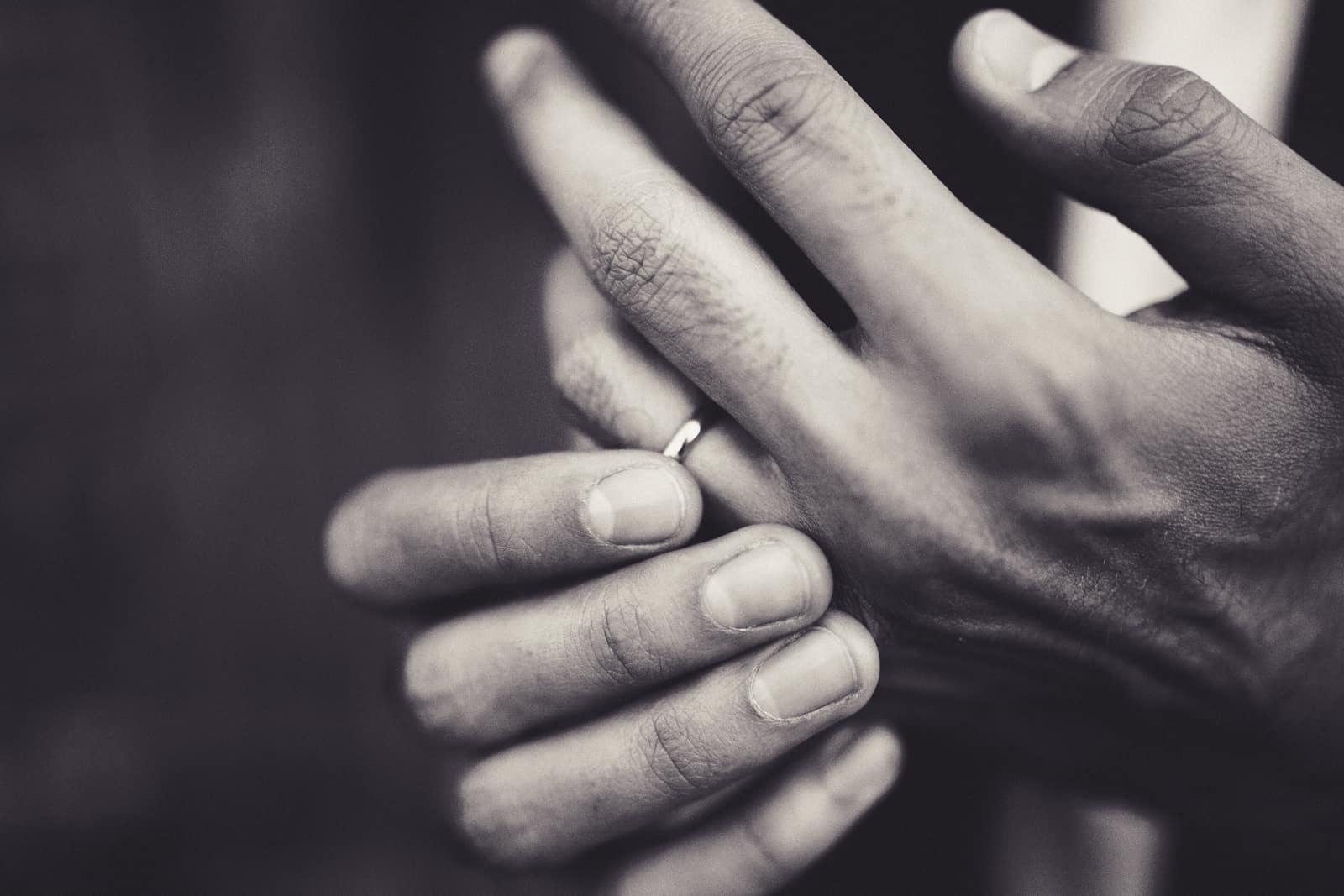 A hand touching a wedding band, in black and white
