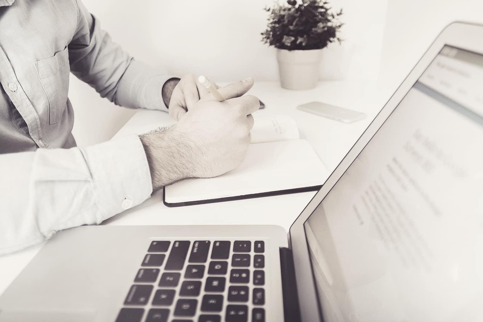 A professional writing notes beside an open laptop